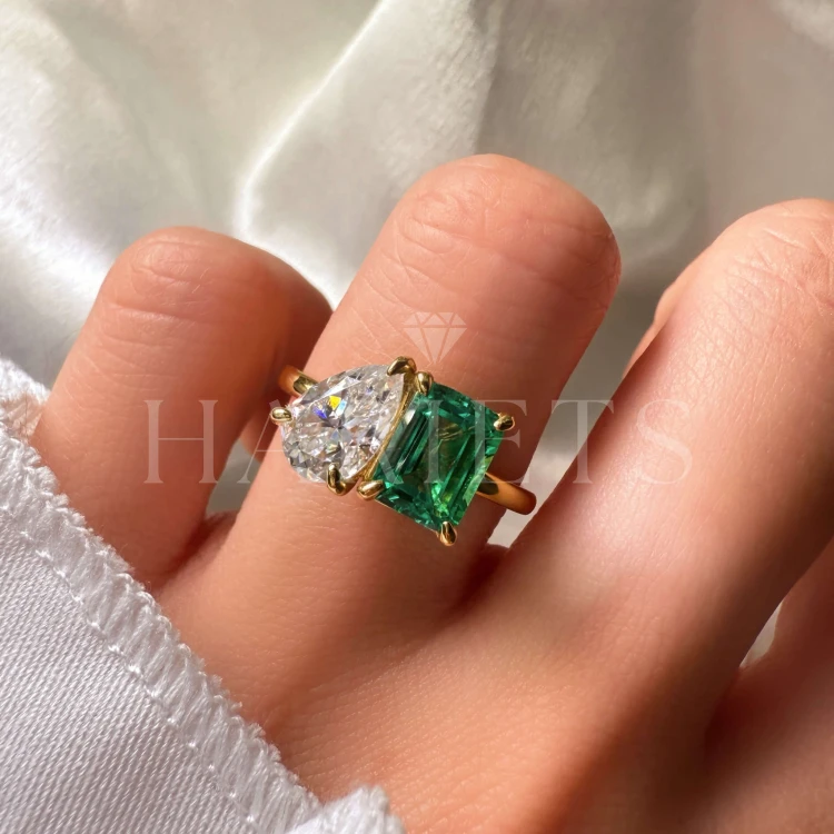 bague-de-fiancailles-toi-et-moi-emeraude-hydrothermale-3-5ct-taille-emeraude-poire-au-doigt-gros-plan-or-jaune-gemini-hariets.