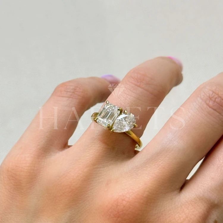 bague-de-fiancailles-toi-et-moi-moissanite-3-5ct-taille-emeraude-poire-au-doigt-gros-plan-or-jaune-gemini-hariets.