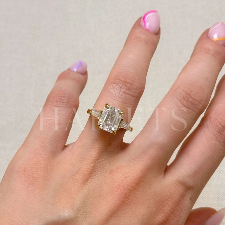 bague-fiancailles-trinity-moissanite-4ct-taille-émeraude-gros-plan-sur-doigt-or-jaune-florence-hariets.