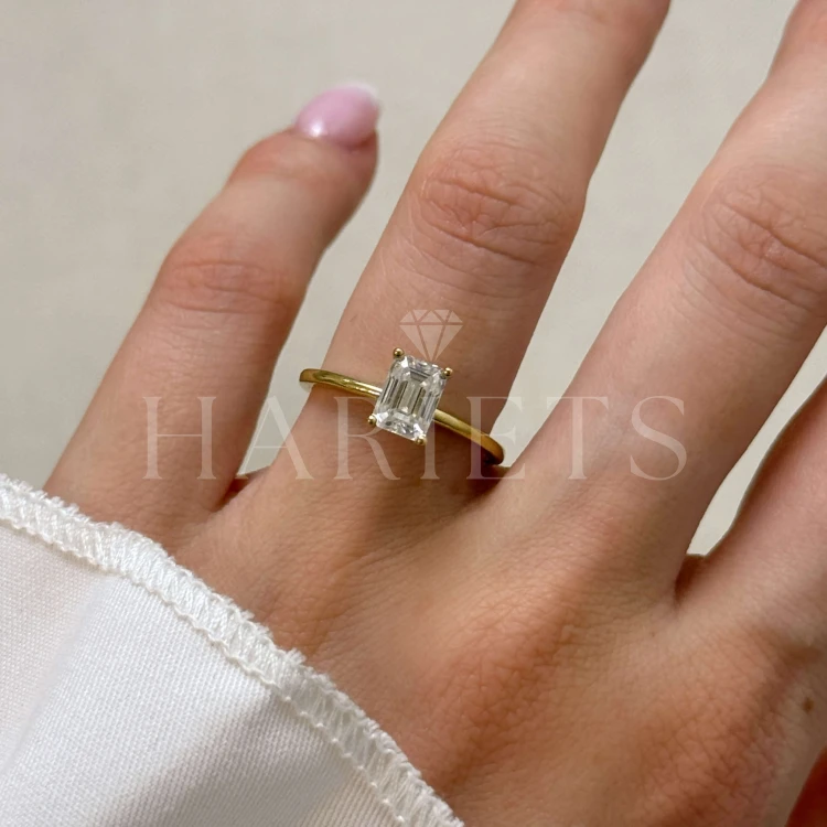 bague-fiancailles-solitaire-verity-moissanite-1ct-taille-émeraude-sur-doigt-or-jaune-hariets.