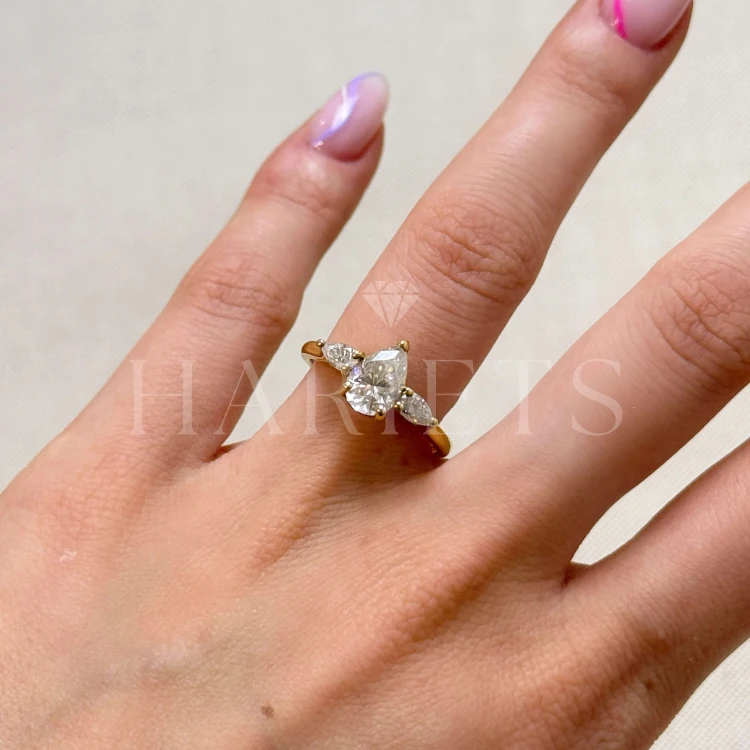 bague-fiancailles-trinity-amara-moissanite-1-5ct-taille-poire-centrale-sur-doigt-or-jaune-hariets.jpg
