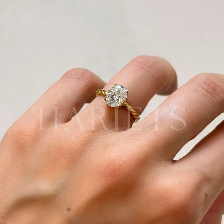 bague-de-fiancailles-bande-torsadee-moissanite-2ct-taille-ovale-au-doigt-gros-plan-or-jaune-twisted-hariets.jpg